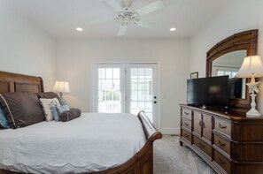 Une chambre à coucher comprenant un lit, une commode, un téléviseur et un ventilateur de plafond.