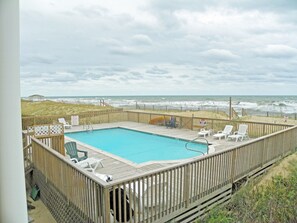 Una terraza de madera con piscina, vistas a la playa y una zona de arena con sillas.