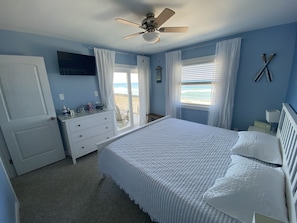 Une chambre à coucher avec un lit, une commode, un ventilateur de plafond et une vue sur l’océan par la fenêtre.