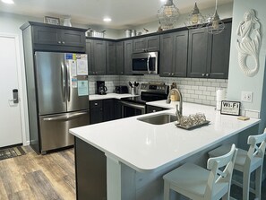 Una cocina moderna con electrodomésticos de acero inoxidable, armarios oscuros y una encimera blanca.