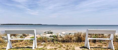 Two white benches facing a beach with a clear sky.