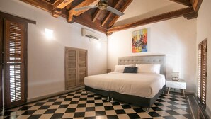 Un dormitorio con piso a cuadros, una cama con ropa de cama blanca, un ventilador de techo y un cuadro en la pared.