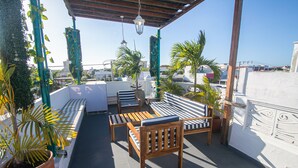 Terraza en la azotea con mobiliario de madera, plantas en macetas y vistas a la ciudad.