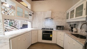 Una cocina con armarios blancos, estufa a gas, horno, microondas y pileta.
