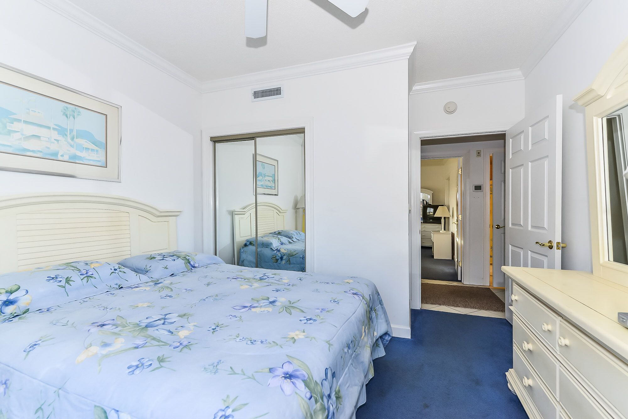 A bedroom with a bed, a dresser, a mirror, and a door leading to another room.