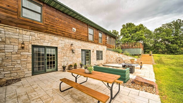 Un patio con una mesa y bancos de madera, muros de piedra y un área de estar verde al aire libre.
