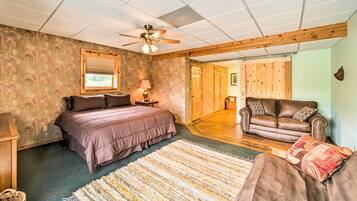 Une chambre à coucher avec un lit, un ventilateur de plafond en bois, un plancher en bois, un canapé en cuir marron et une grande fenêtre.