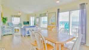 A spacious living area with a wooden dining table, white chairs, a blue sofa, and a television. - Krabby Patty – Oceanfront Family Fun (Topsail Beach)