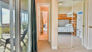 A room with a view of the ocean, a wooden bunk bed, and a sliding door leading to another room. - Krabby Patty – Oceanfront Family Fun (Topsail Beach)