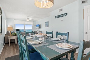 A dining area with a table set for four, a ceiling fan, and a view of the ocean.