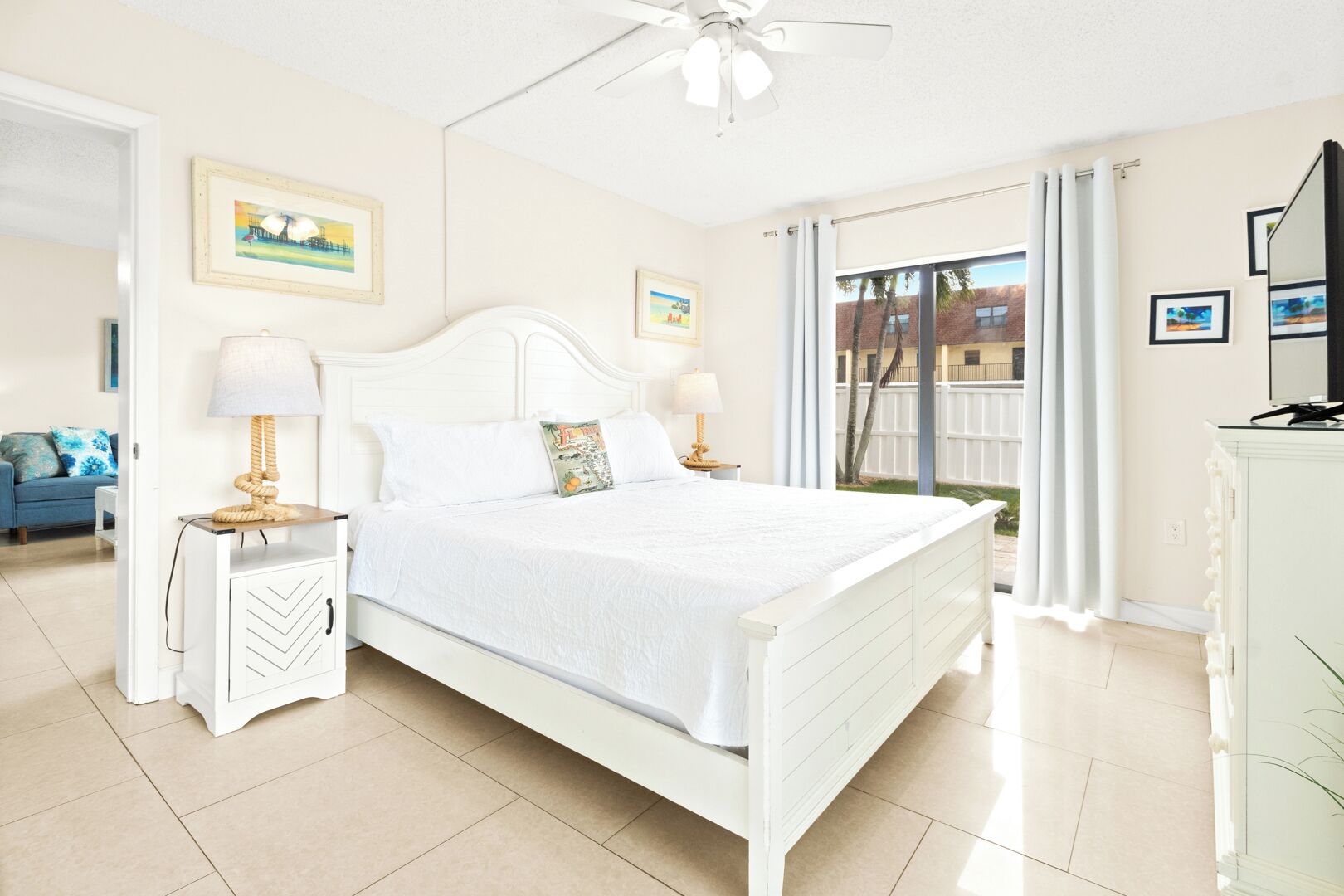 Um quarto espaçoso com uma cama grande, duas mesas de cabeceira com luminárias, um ventilador de teto e vista para o exterior através de uma porta de vidro deslizante.