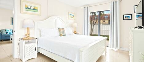 Um quarto espaçoso com uma cama grande, duas mesas de cabeceira com luminárias, um ventilador de teto e vista para o exterior através de uma porta de vidro deslizante.