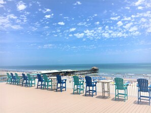 Une terrasse avec des chaises et des tables donnant sur une plage et une jetée.
