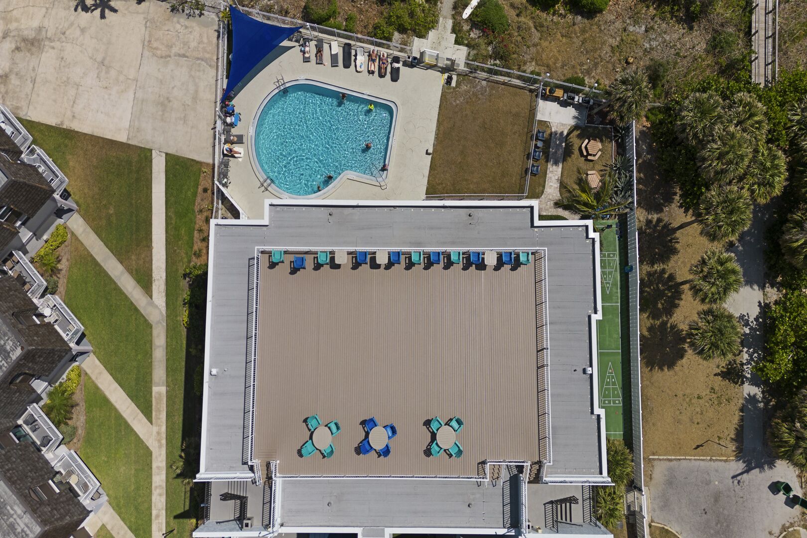 An aerial view of a building with a swimming pool, outdoor seating, and a tennis court.