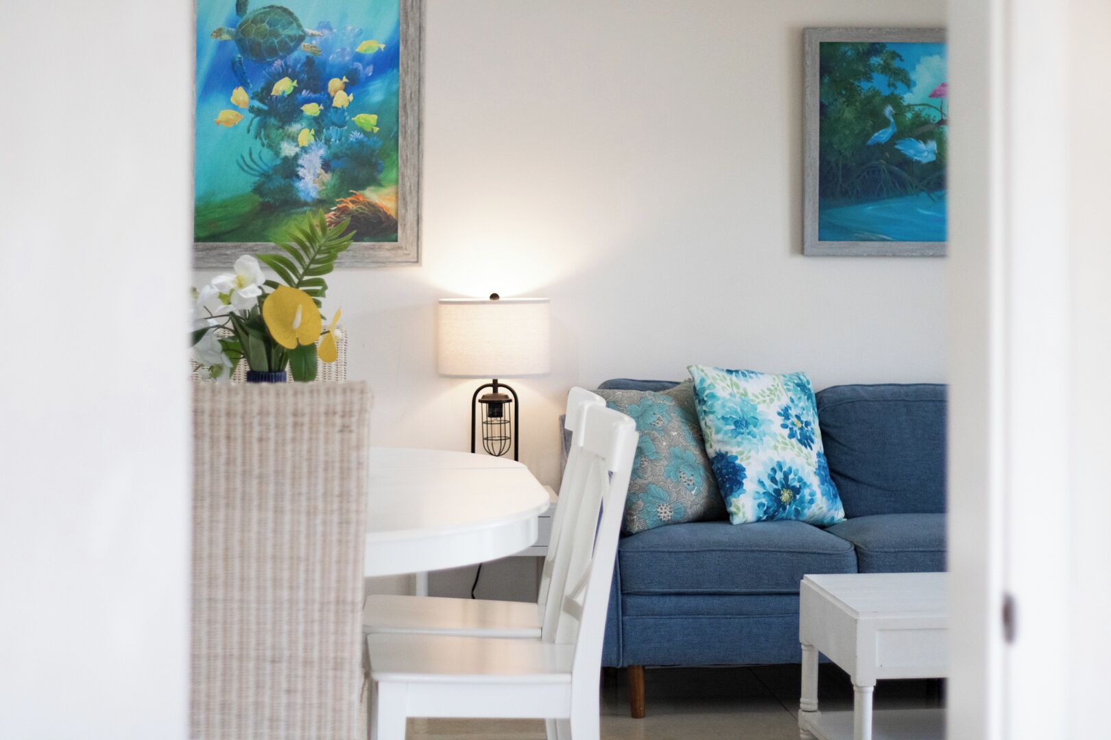 Ein Wohnzimmer mit einem blauen Sofa, weißen Sesseln, einem runden Tisch und zwei Bildern an der Wand.