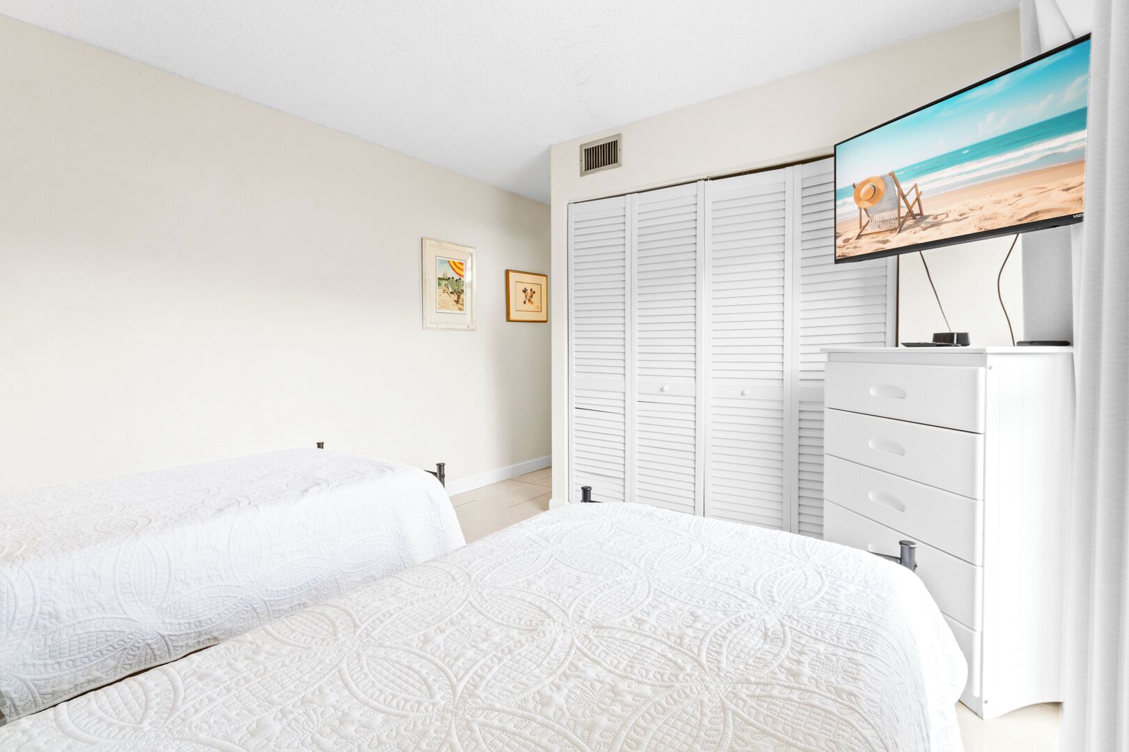 A bedroom with two beds, a TV on the wall, a wardrobe, and a dresser.