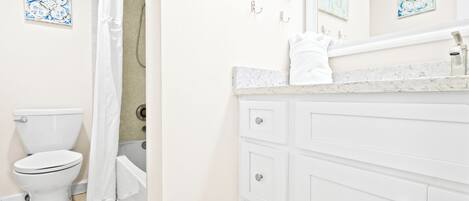 A bathroom with a toilet, shower, and a vanity with a mirror.