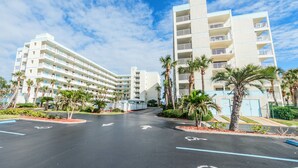 Een hotel met meerdere verdiepingen, een centrale binnenplaats, palmbomen en een heldere lucht.