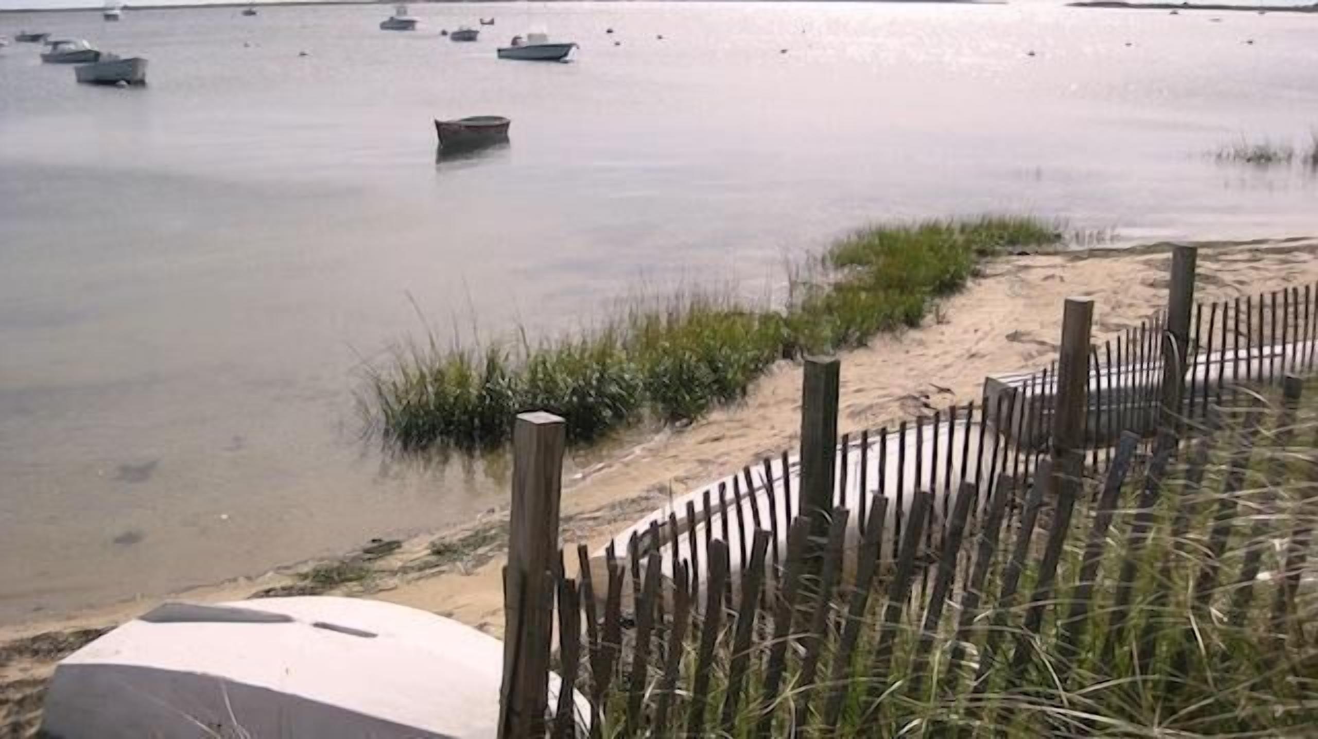 Een zanderig strand met een houten hek en verschillende boten in het water.