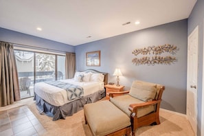 A bedroom with a bed, a chair, a nightstand, and a window.