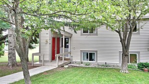 A two-story house with a front porch, a red door, and a small front yard. - Leelanau County, 4-brm 4-bath. A/C, Pool, 5 mins to Lk Michigan Beach (Cedar)