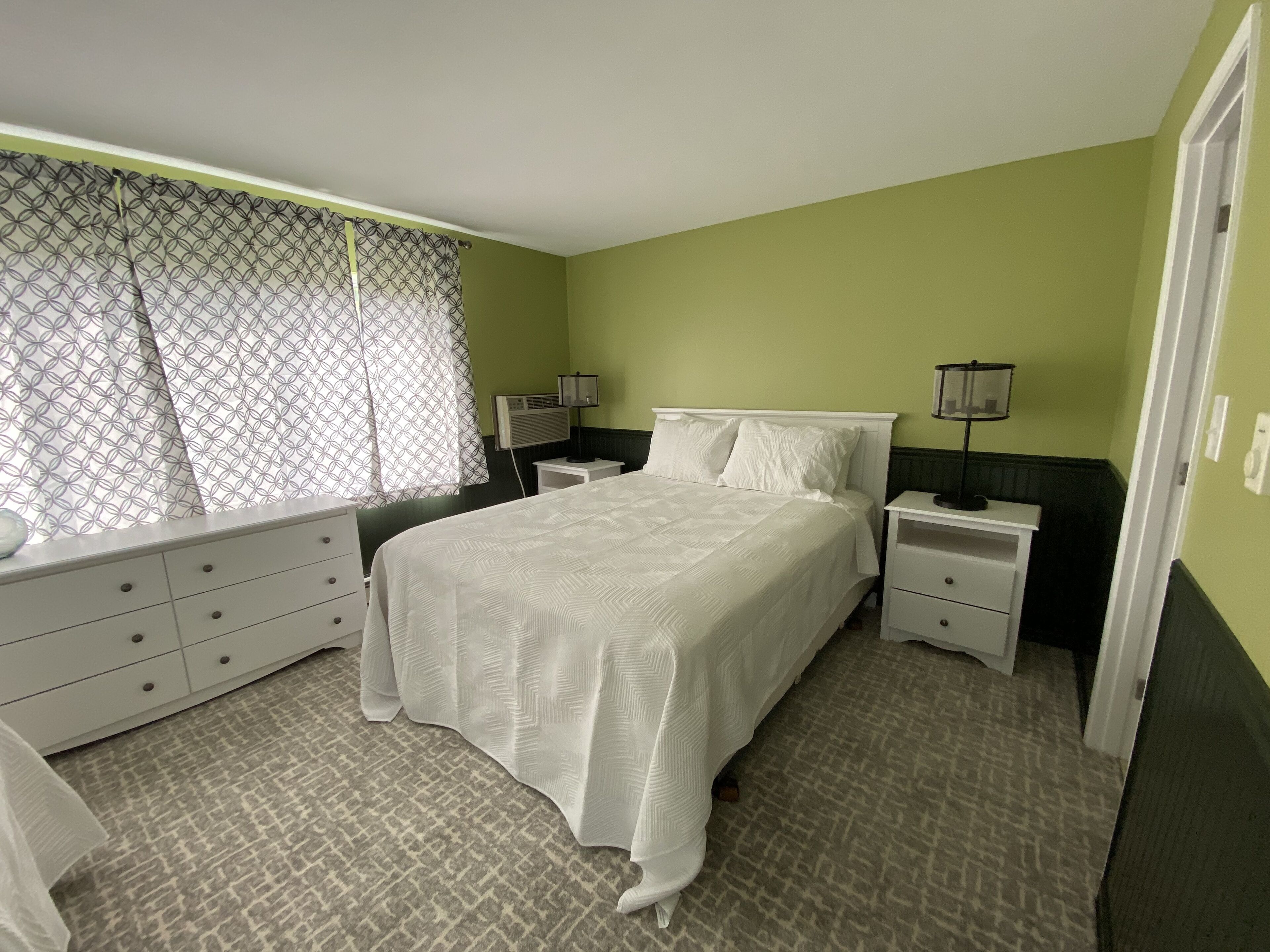 A bedroom with a bed, bedside tables, a dresser, and a window with patterned curtains.