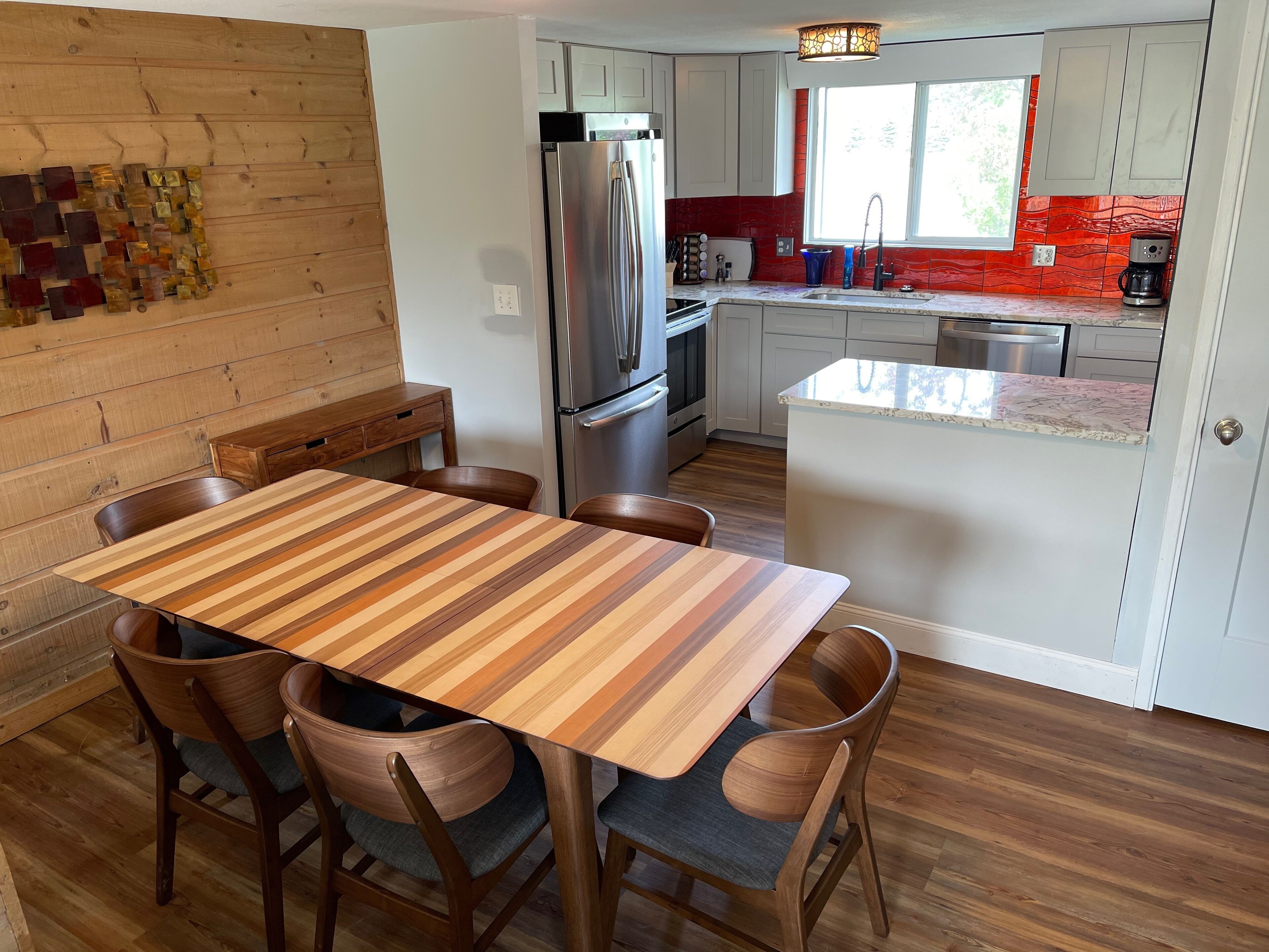 Een moderne keuken met een centraal eiland, roestvrijstalen apparatuur en een houten eettafel met stoelen.