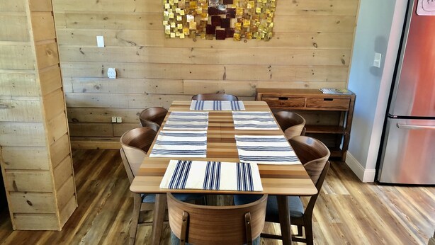 A wooden dining table with striped placemats, surrounded by wooden chairs with cushioned seats. - Leelanau County, 4-brm 4-bath. A/C, Pool, 5 mins to Lk Michigan Beach (Cedar)