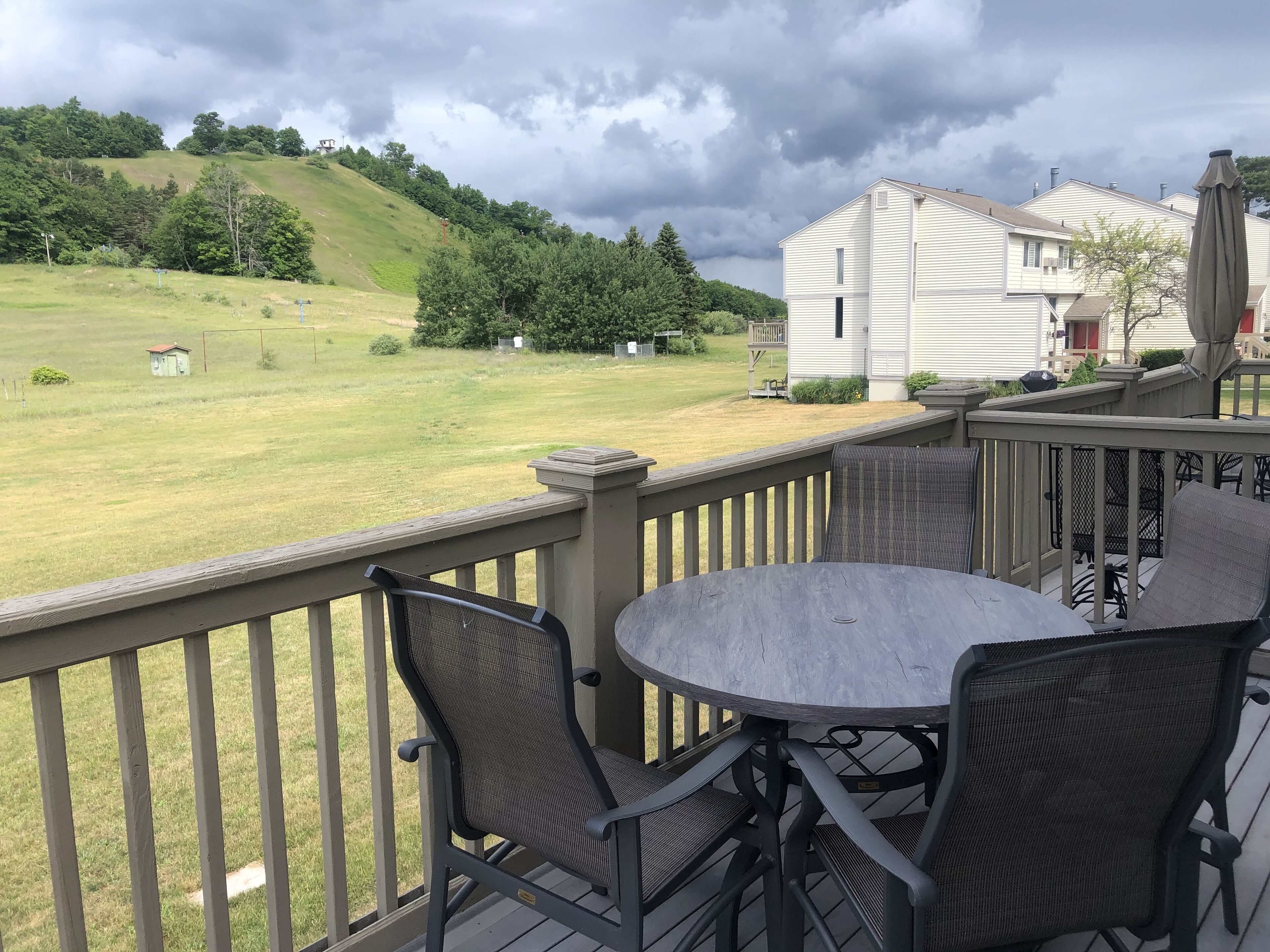 A balcony with a table and chairs overlooking a grassy yard and a hill with trees.