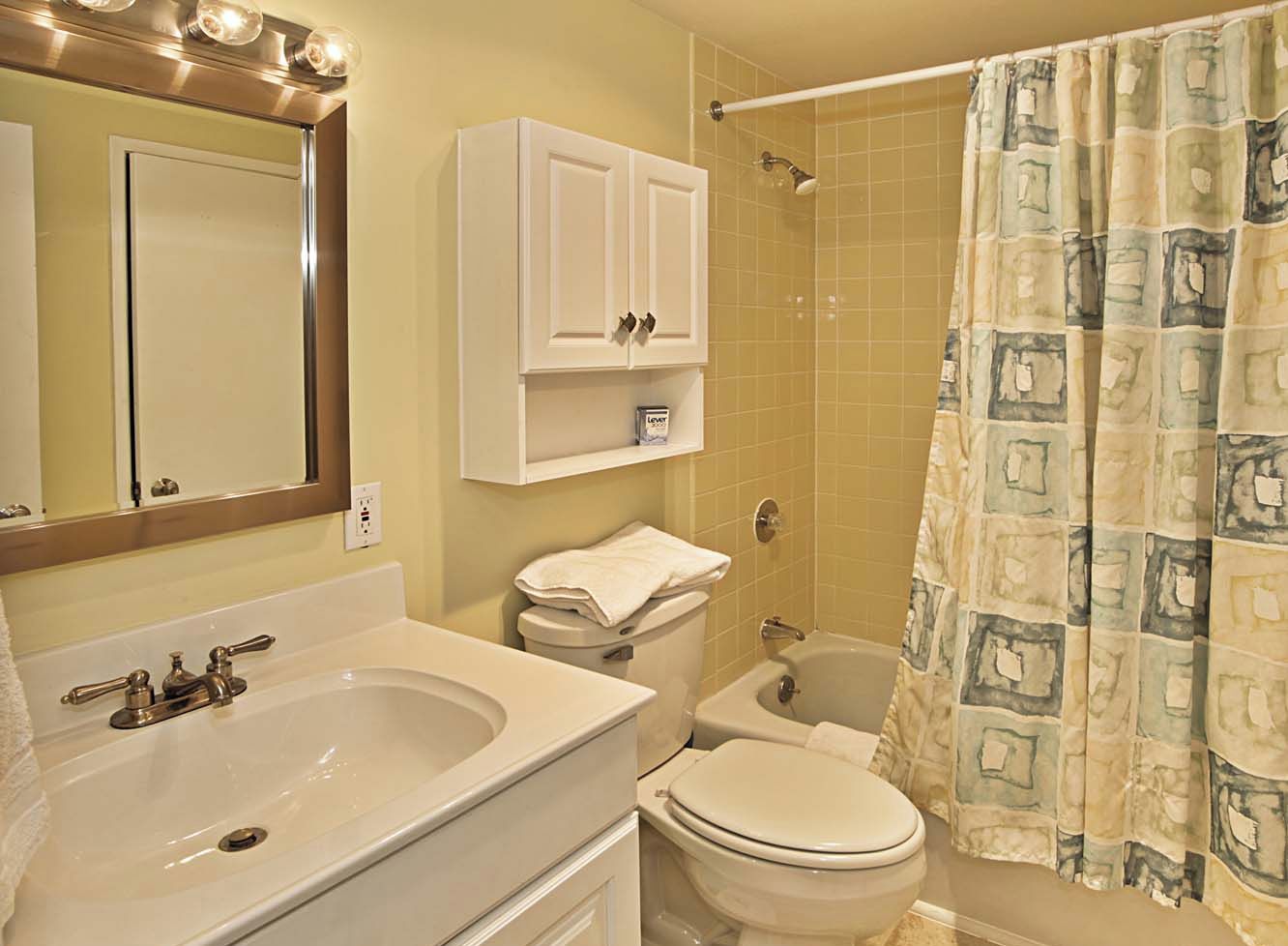 A bathroom with a sink, mirror, cabinet, toilet, and shower curtain.