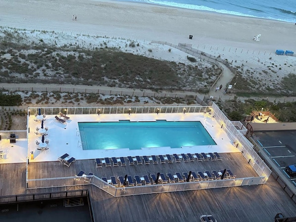 A pool area with lounge chairs and a pool, surrounded by a deck and a fence.