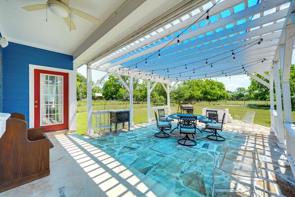 Relax in a serene outdoor space with a round table, comfortable chairs, and a wooden bench, set beneath a shaded pergola.