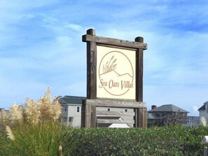 Schild für Sea Oats Villas mit einem Logo aus Berg und Wellen, umgeben von Grünflächen und Gebäuden.