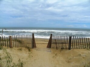 Ein Zugang zum Strand mit einem Holzzaun und einem sandigen Weg zum Meer.