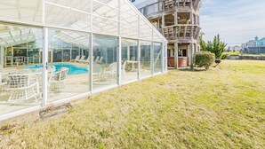 Un espace piscine entièrement vitré, doté de chaises longues, d’une terrasse en bois et d’un immeuble à plusieurs étages avec des balcons.