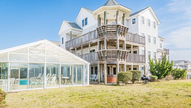 Une grande maison à plusieurs étages, dotée d’un patio entièrement vitré et d’un espace extérieur aménagé pour s’asseoir.