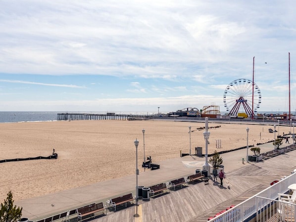 A beach with a pier, a Ferris wheel, and a boardwalk with benches and street lamps.