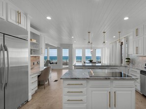 A modern kitchen with white cabinetry, a large island, and a view of the ocean.