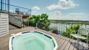 Une terrasse en bois avec un jacuzzi, un banc blanc et une vue sur une rivière et des arbres.