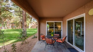 Une terrasse extérieure avec une table et des chaises, un pot de fleurs et, en arrière-plan, une pelouse et un bâtiment.