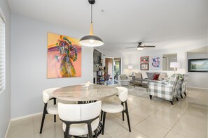 A modern living room with a dining area, a ceiling fan, and a large painting on the wall.
