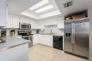 A modern kitchen with white cabinets, stainless steel appliances, a skylight, and a built-in dishwasher.