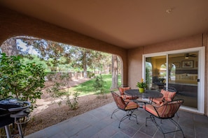 A covered patio with a table and chairs, a grill, and a view of a landscaped yard.