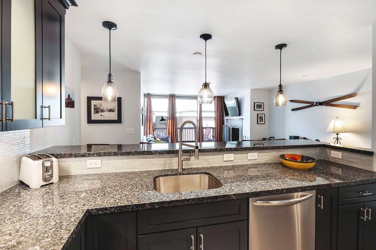 A modern kitchen with granite countertops, stainless steel appliances, pendant lighting, and a visible dining area.