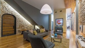 Una sala de estar moderna con una pared de piedra, una puerta de madera, un sofá gris, una mesa de centro de vidrio y una lámpara colgante.