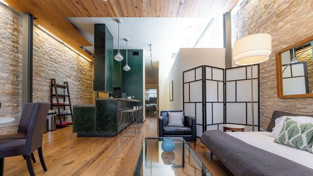 Un interior moderno con suelo de madera, una mesa de centro de vidrio, un sofá y una zona de estar con una mesita.