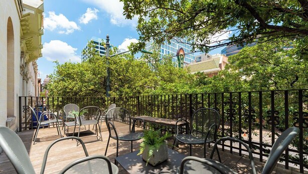 An outdoor seating area with metal chairs and tables, surrounded by a black metal fence, with trees and buildings in the background. - Luxury Stay | Views, Game Room & Chef’s Kitchen (Austin)