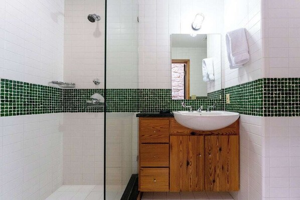A bathroom with a glass shower enclosure, a wooden vanity with a sink, and green-tiled walls.