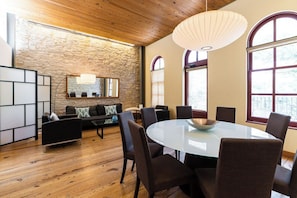 A modern dining area with a round glass table surrounded by chairs, a stone wall, and large windows.