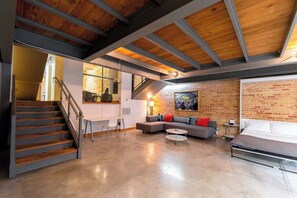 A spacious loft-style living area with a staircase, a sofa set, a dining table, and a large window.